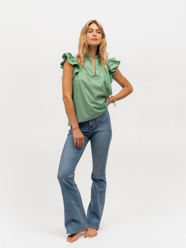 Woman wearing jeans and a light green ruffle sleeve shirt