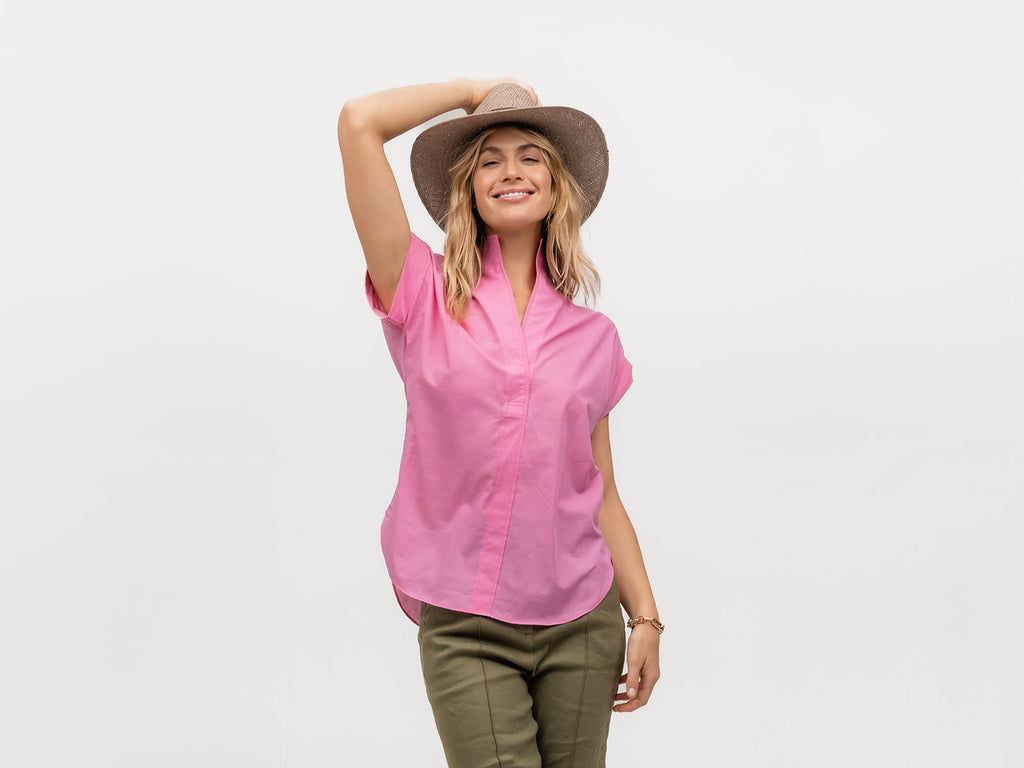Smiling woman wearing a hat and a hot pink designer short sleeve top