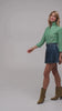 Beautiful woman modeling a green designer blouse with a short denim skirt and ankle boots